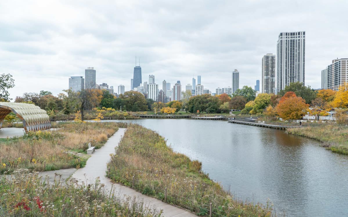 Scenic view over pond in Lincoln park, with grassy walking trails in the foreground and the Chicago skyline in the background