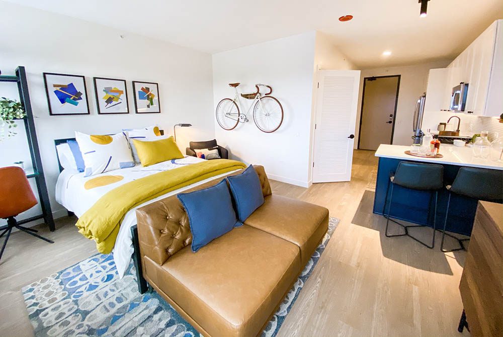 Modern hotel-style apartment with queen size bed, couch, bicycle on wall, and dining table