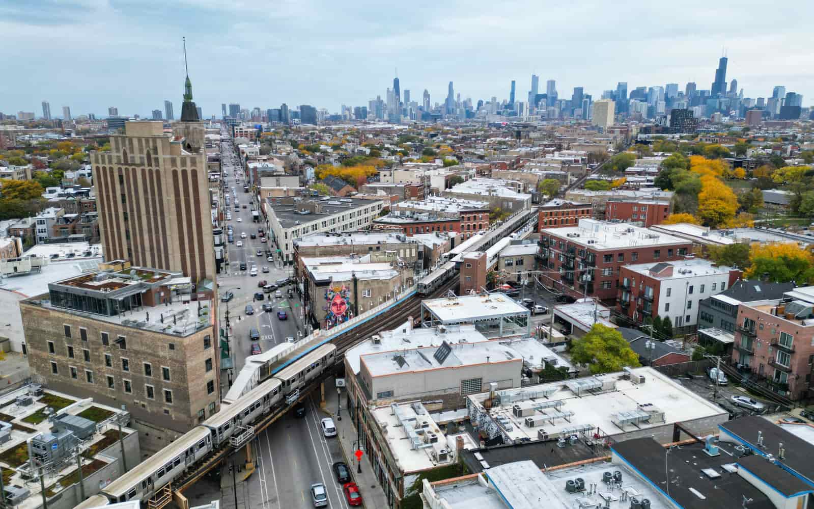 Overhead view of busy intersection in Wicker Park, with CTA L trains crossing and downtown Chicago skyline in the background