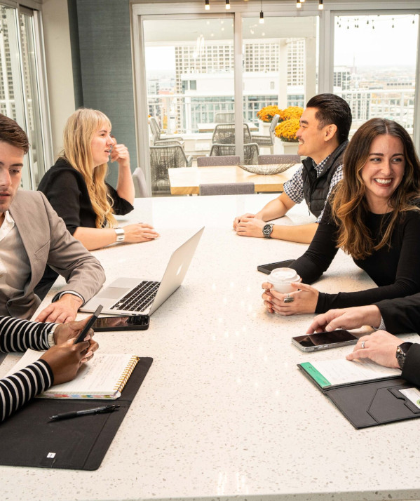 Group of business casual coworkers seated at a conference table, smiling and chatting as they work.
