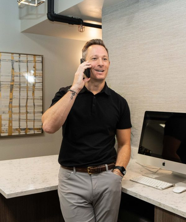 Leasing agent in business casual attire, standing in an office area and smiling while on a mobile phone call