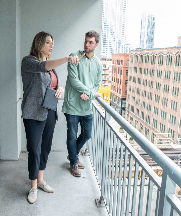 Leasing agent standing on an apartment balcony with her client as she points out neighborhood landmarks