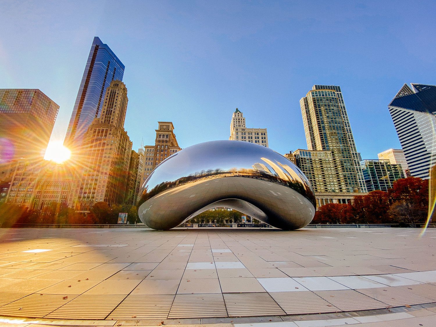 Chicago skyline with sunset shining through buildings behind the famous Bean.