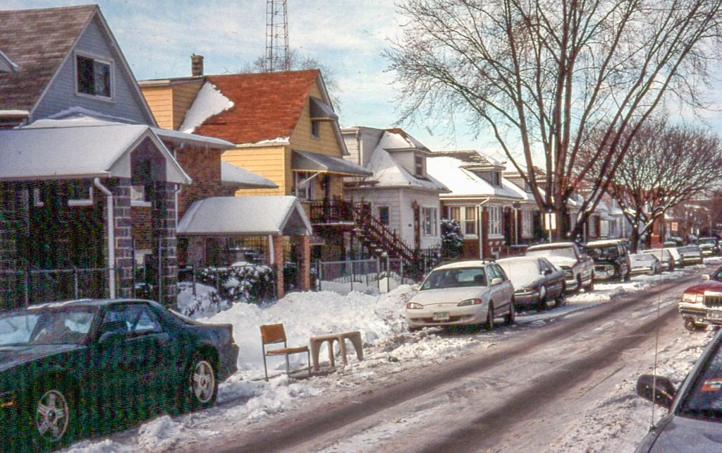 A photo of cars on a snowy Chicago block and a spot saved using furniture, DIBS style