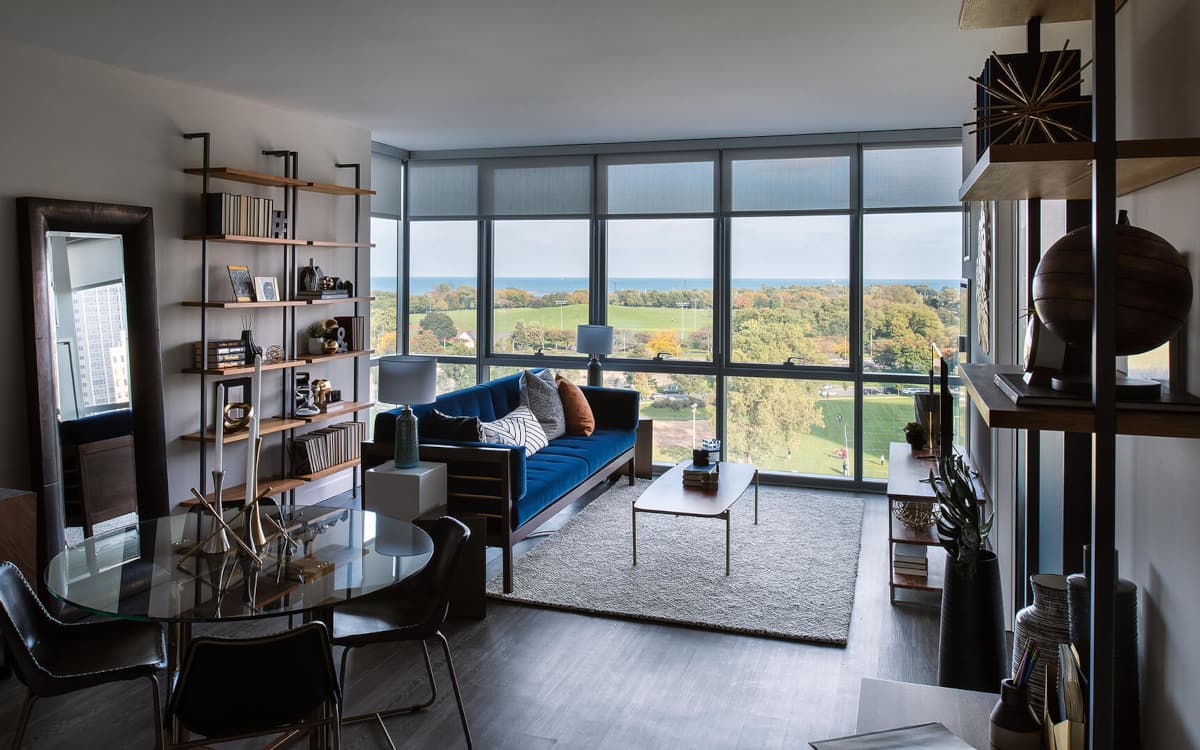 Furnished living area at Eight Eleven Uptown with floor to ceilings window revealing a gorgeous view of a large park and Lake Michigan