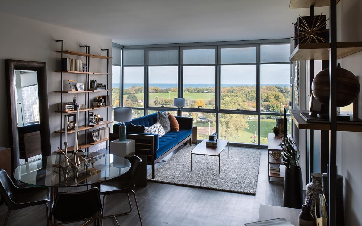 Furnished living area at Eight Eleven Uptown with floor to ceilings window revealing a view of a large park and Lake Michigan