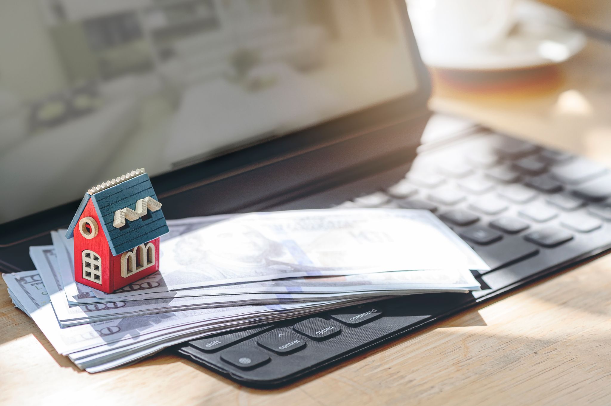 A small model house sits on a stack of U.S. dollar bills placed on a tablet keyboard, symbolizing net effective rent for real estate.